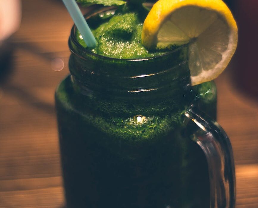 close up photography of clear glass mason jar mug with green juice and sliced citrus toppings