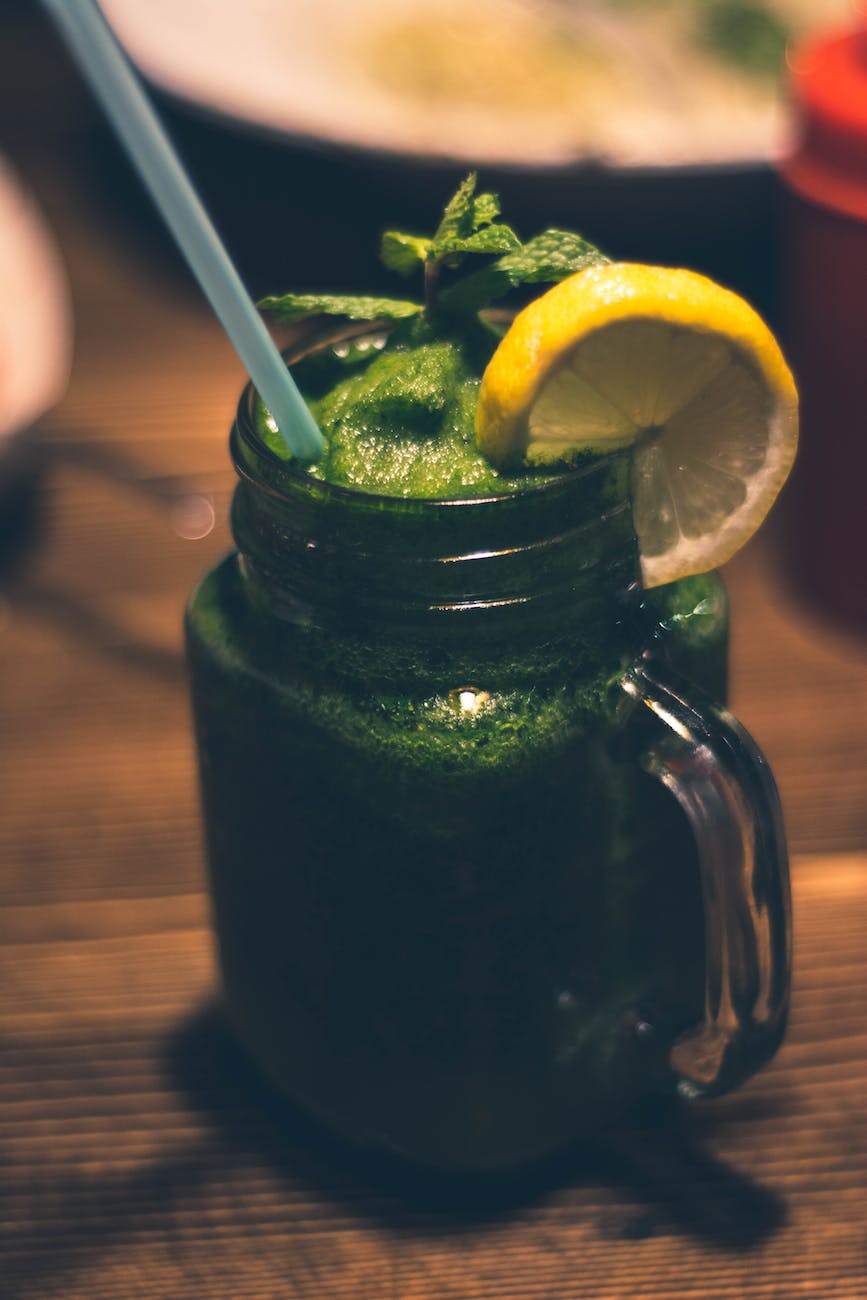 close up photography of clear glass mason jar mug with green juice and sliced citrus toppings